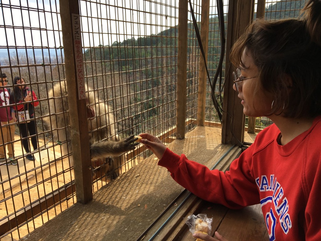 Vrouw in rode trui geeft eten aan een aap in Japan.