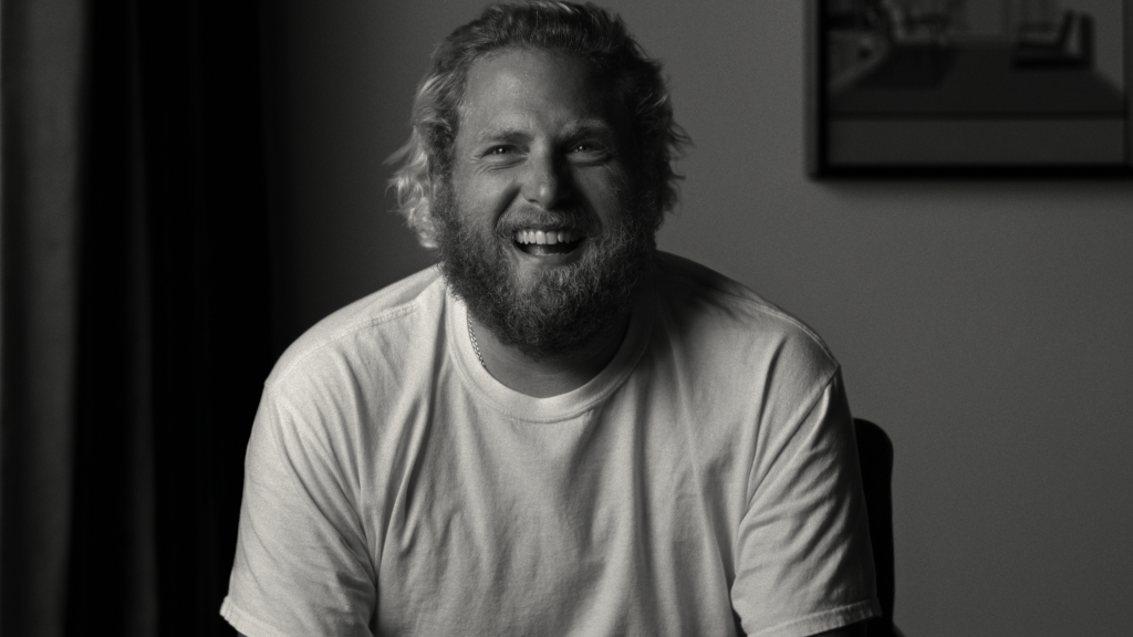 A black and white still of Jonah Hill similing, wearing a white tshirt, in the Netflix documentary Stutz.