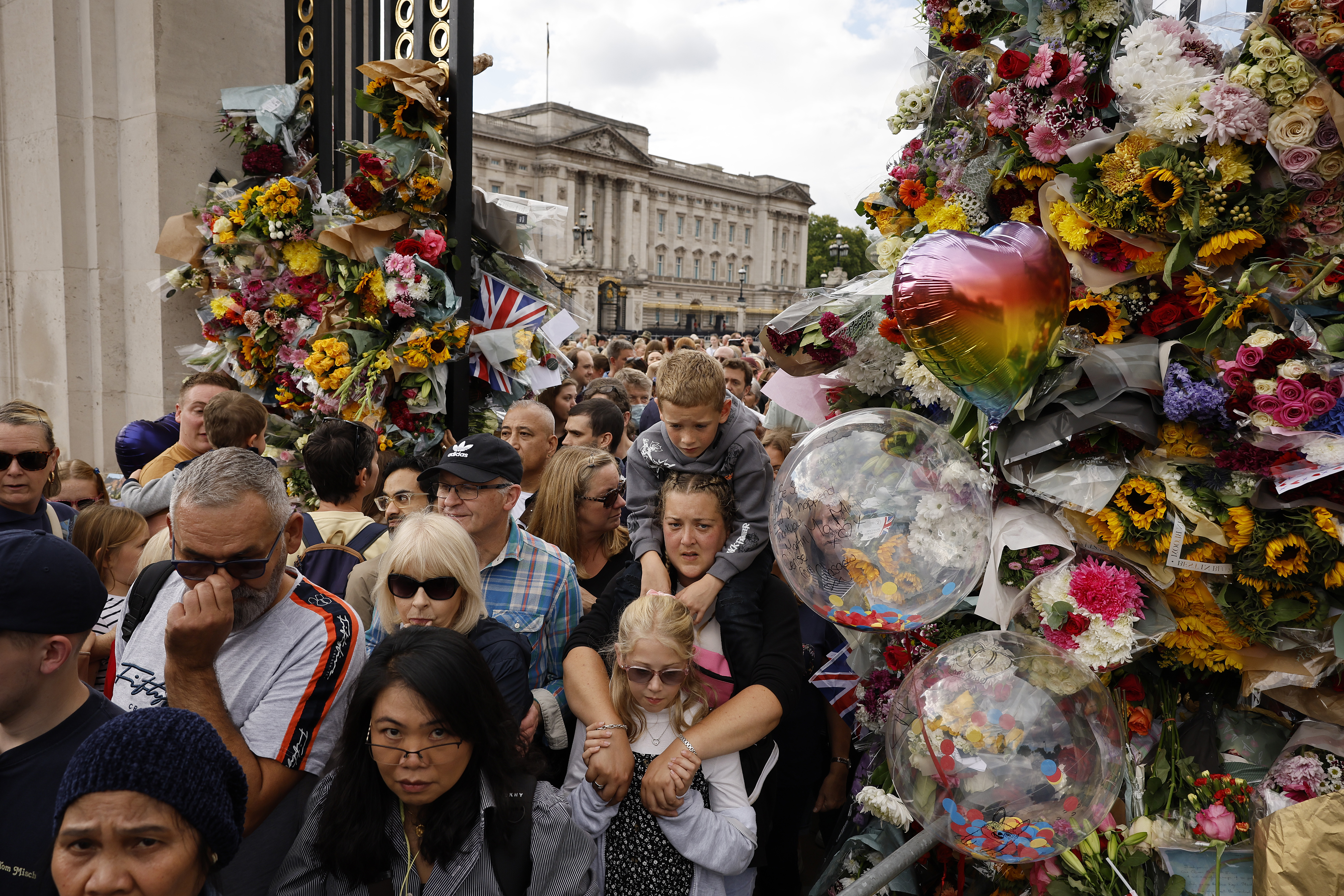 Eine Menschenmenge geht zwischen Blumen und Luftballons durch einen Toreingang