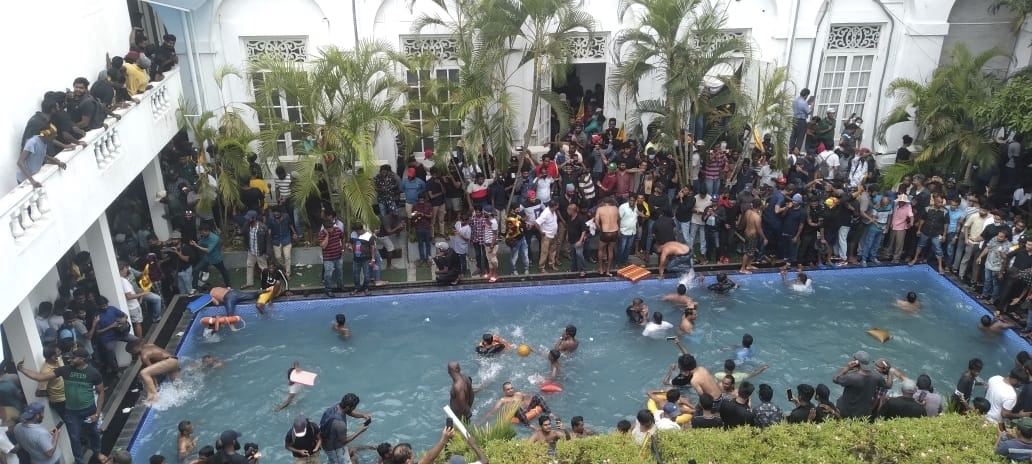 Eine Menschenmenge steht um das Schwimmbecken eines imposanten Anwesens