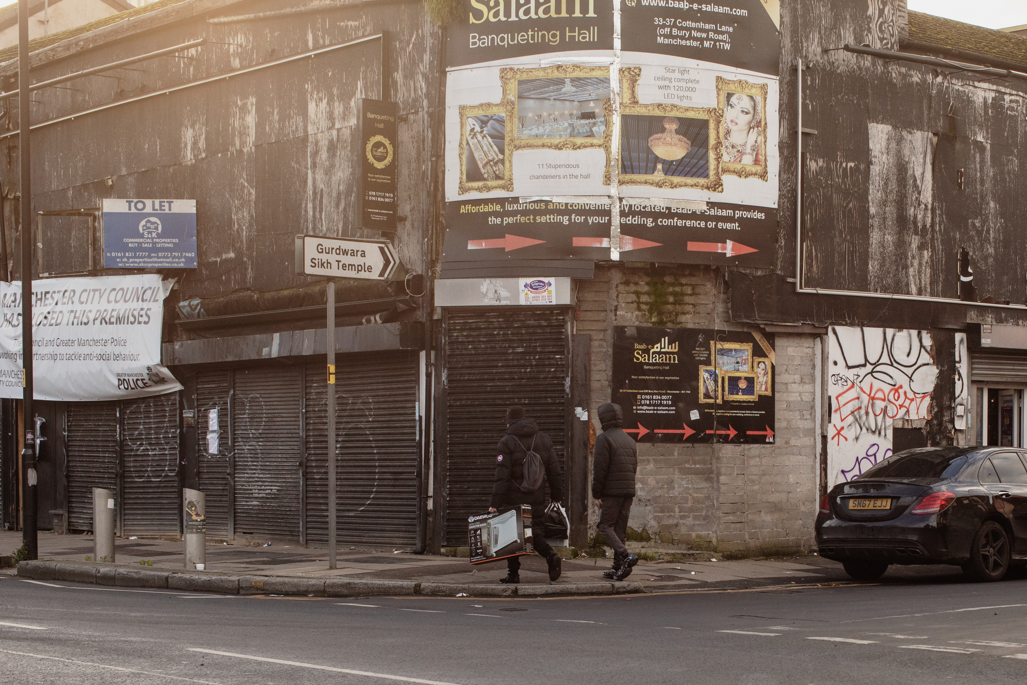 Two people with bags in hand walk down an empty street with shuttered stores.