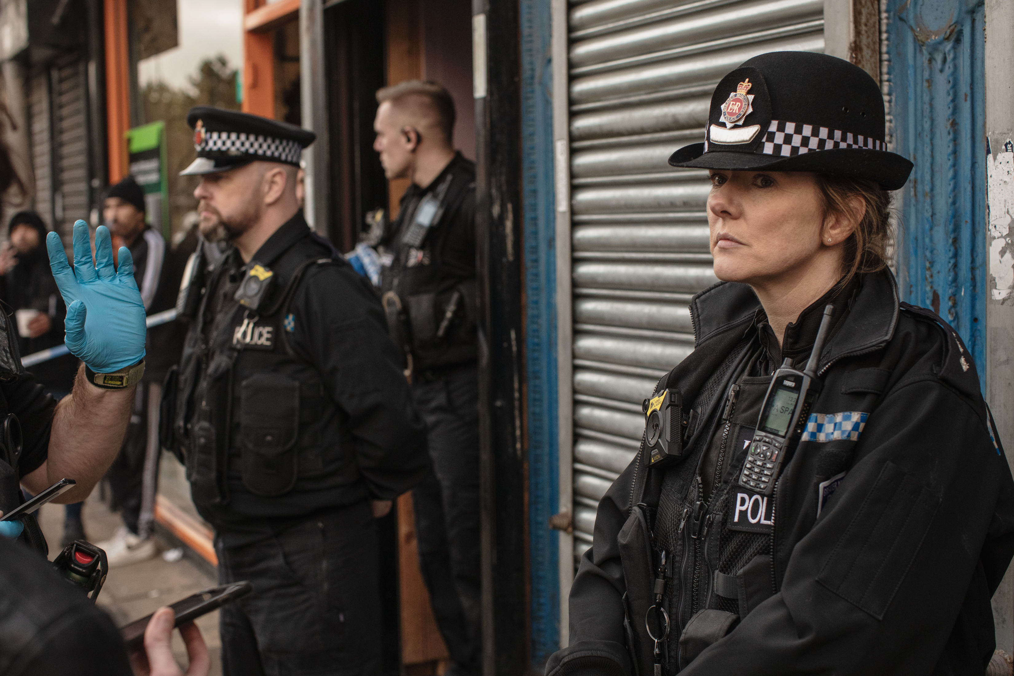 Police officers stand outside of a shuttered store, a female officer stands in the foreground.