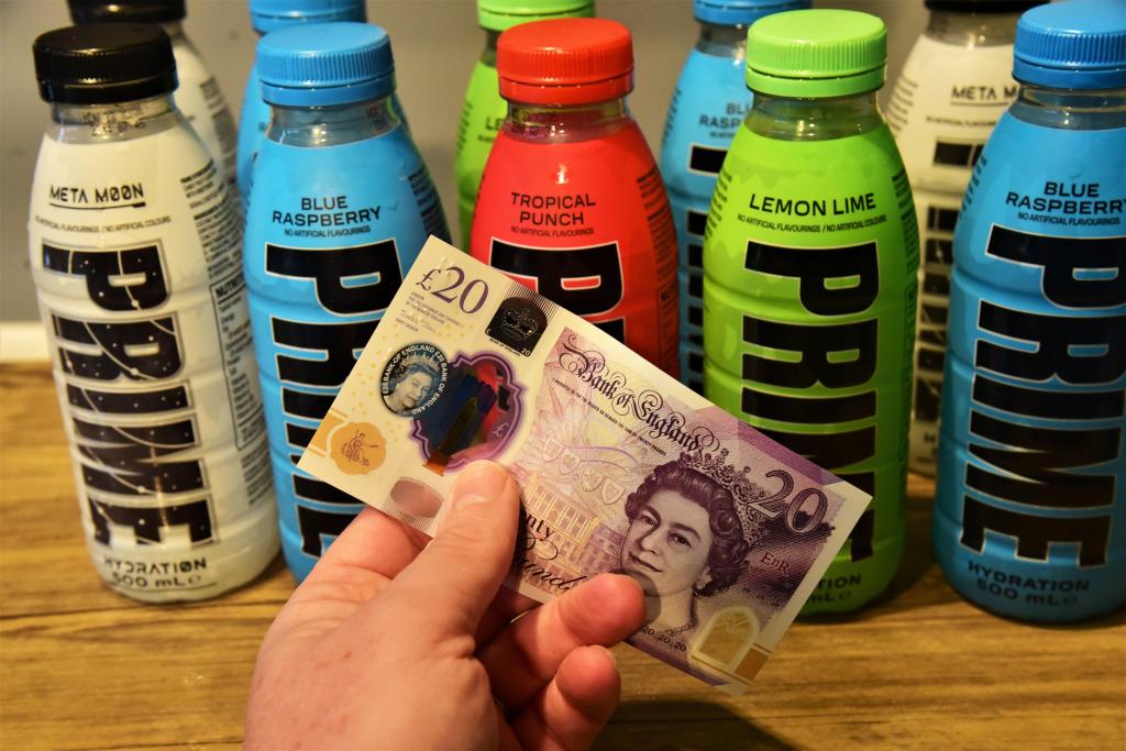 A £20 note held in front of a row of Prime energy drink bottles