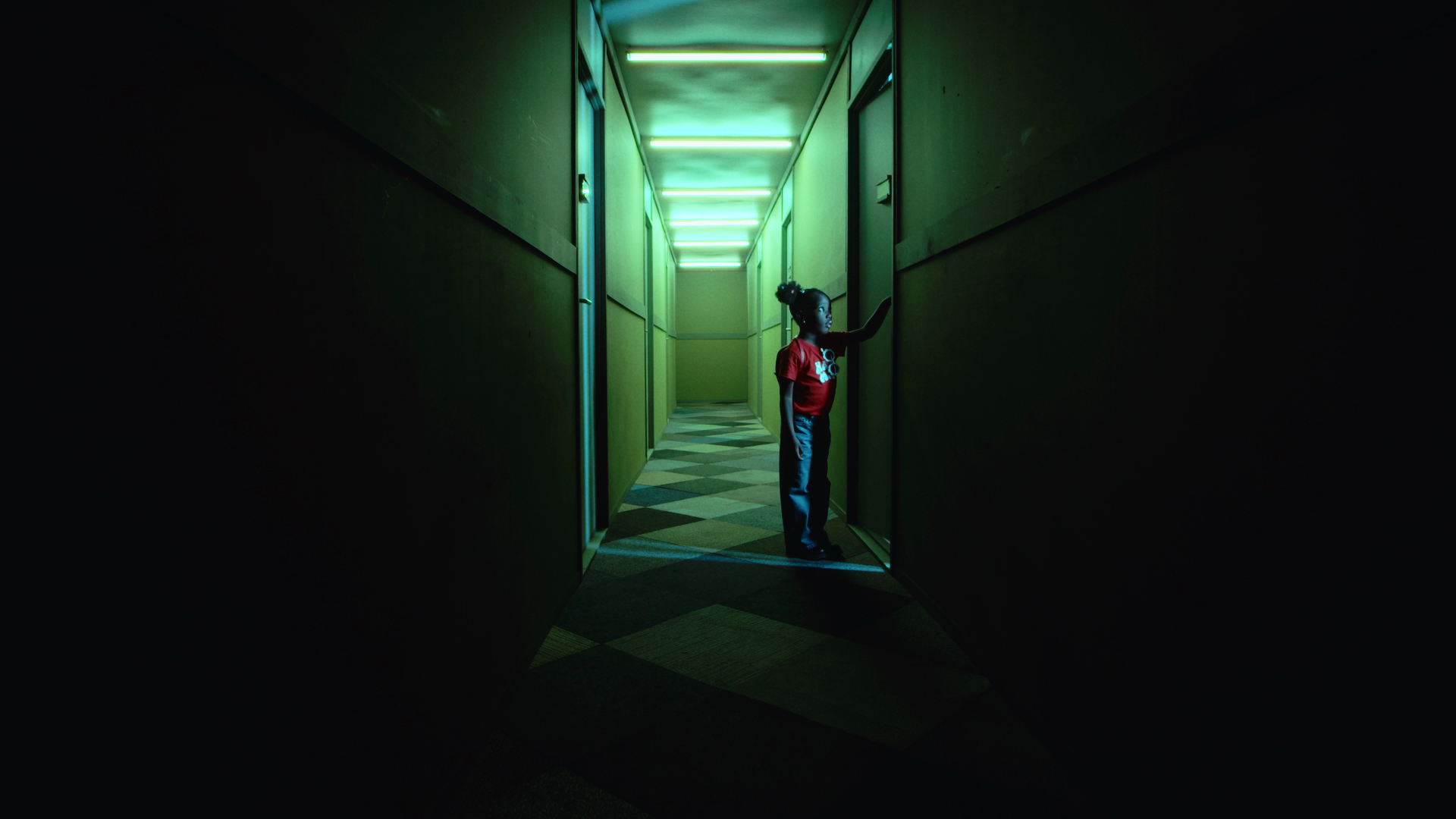 Elisabetta Agyeiwaa – photo of a young girl in a dark corridor lit by green overhead lights, looking through a narrowly opened door.