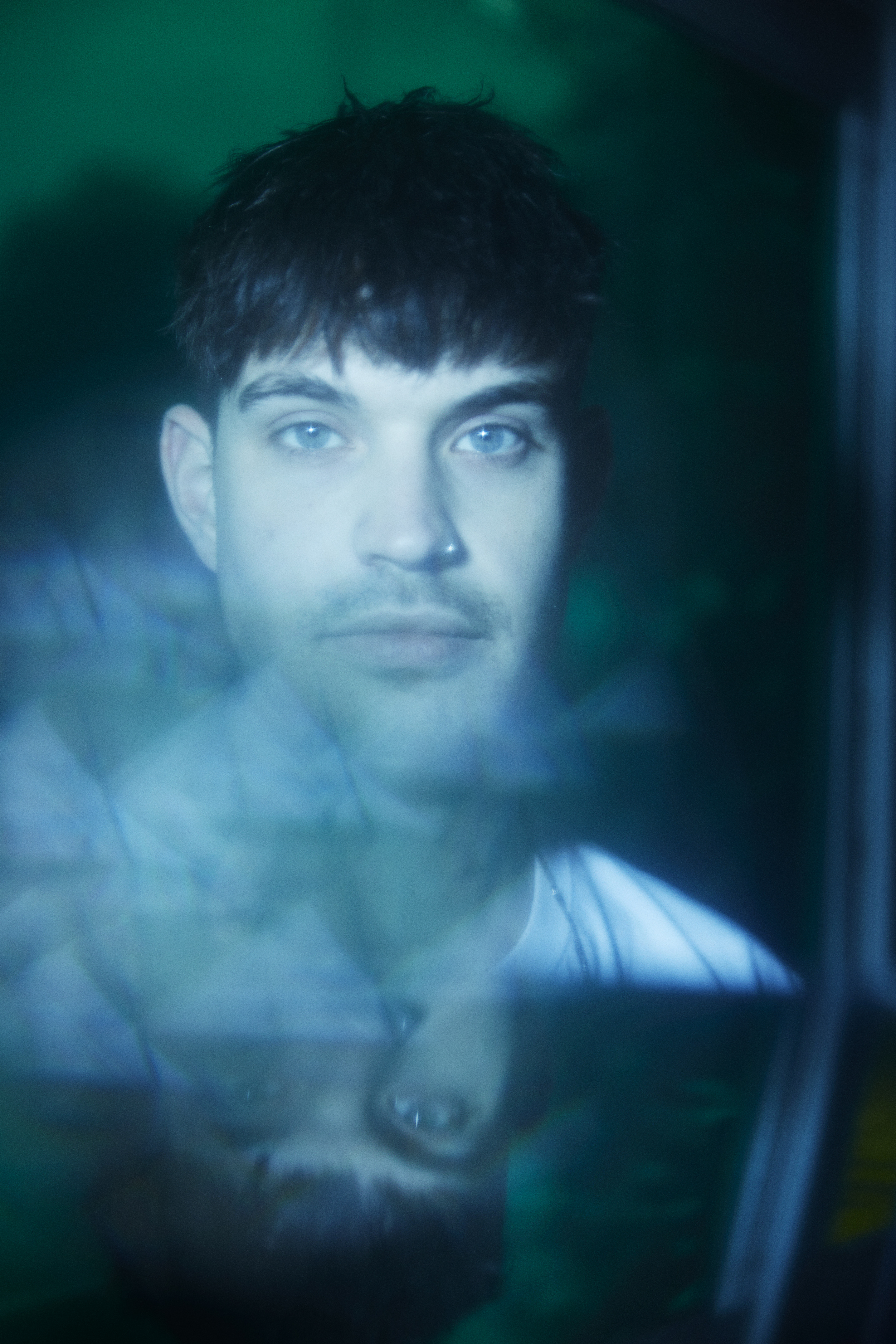 Nick - blurry portrait of a man with short dark hair, blue eyes and a nose piercing looking at the camera