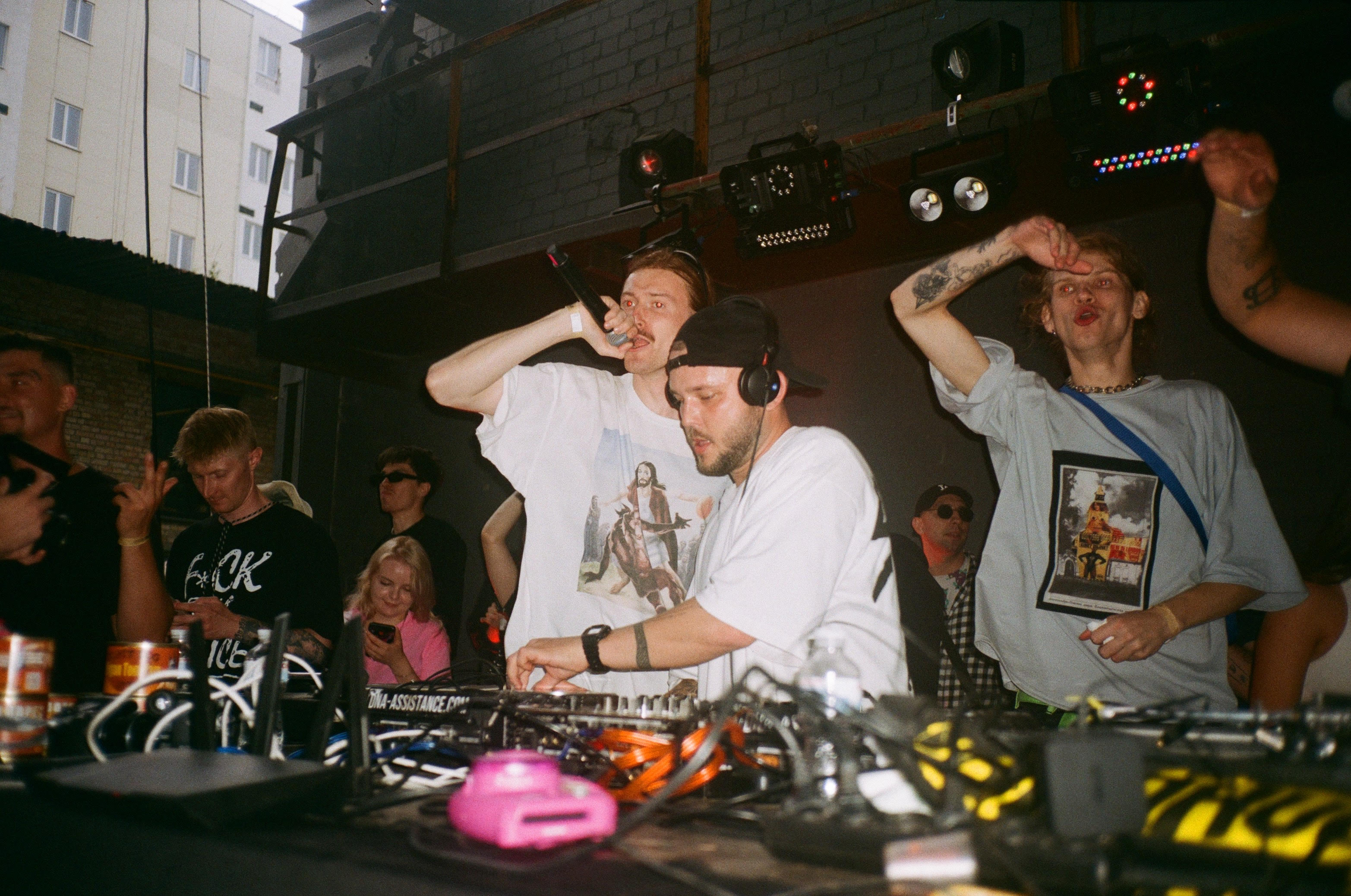 BRUDNIY PES Ukraine party – Dj set with one man spinning and one singing, both wearing white shirts, surrounded by a crowd of people jumping up.