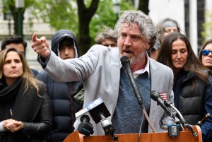 Photo of Del Bigtree at an outdoor lectern with a crowd behind him