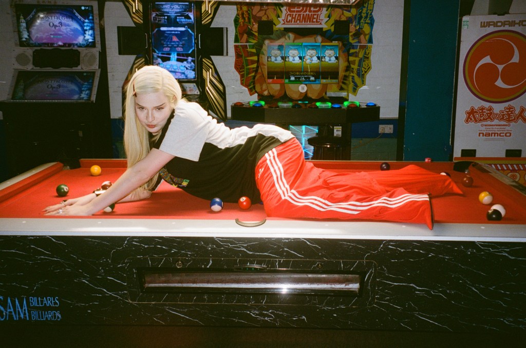 Kim Petras lays on a red top pool table in a seductive pose. Arcade marchines ca