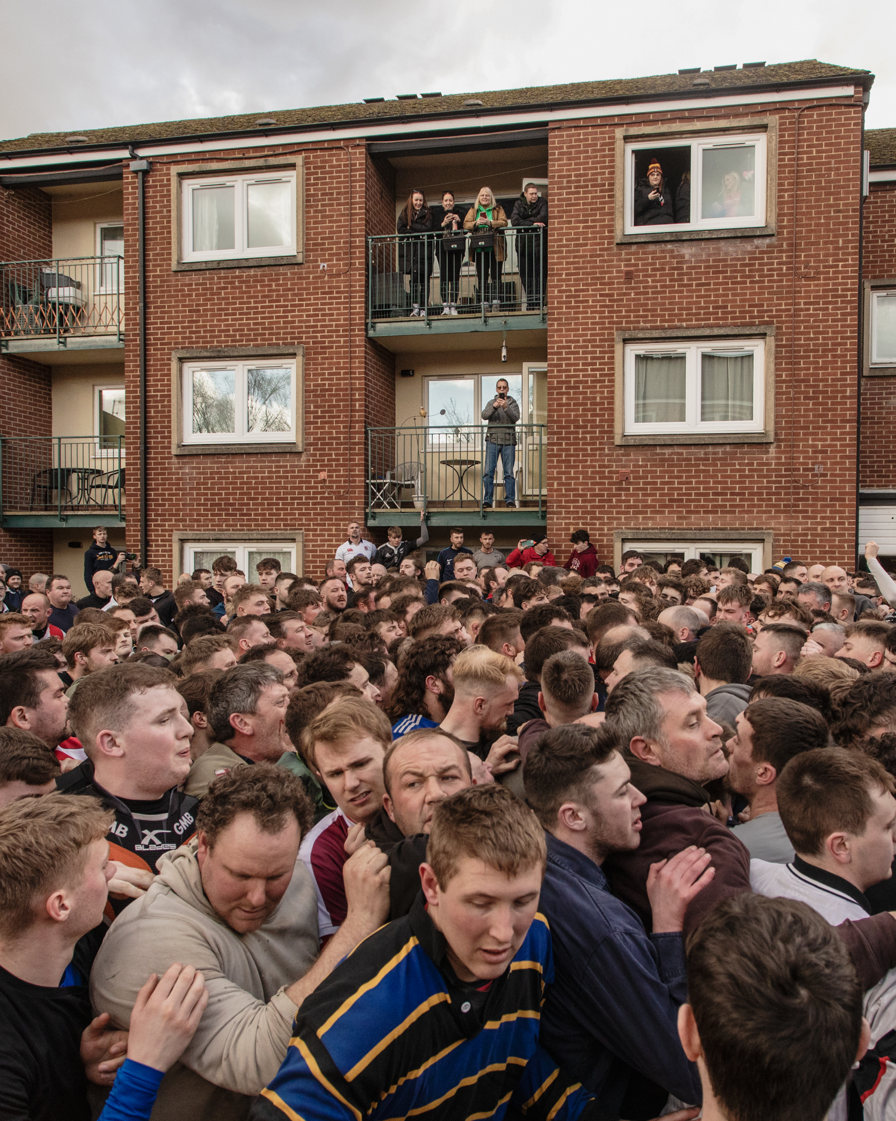 Dozens of men fill the streets and the foreground, a few people look over from their flats in the background.