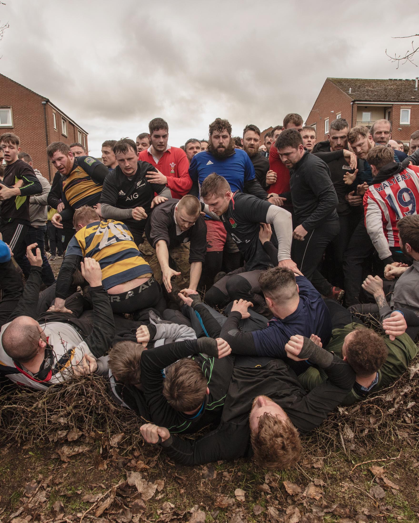 A few men fall over on their backs as a bunch of men look over them, some are trying to help them get up.