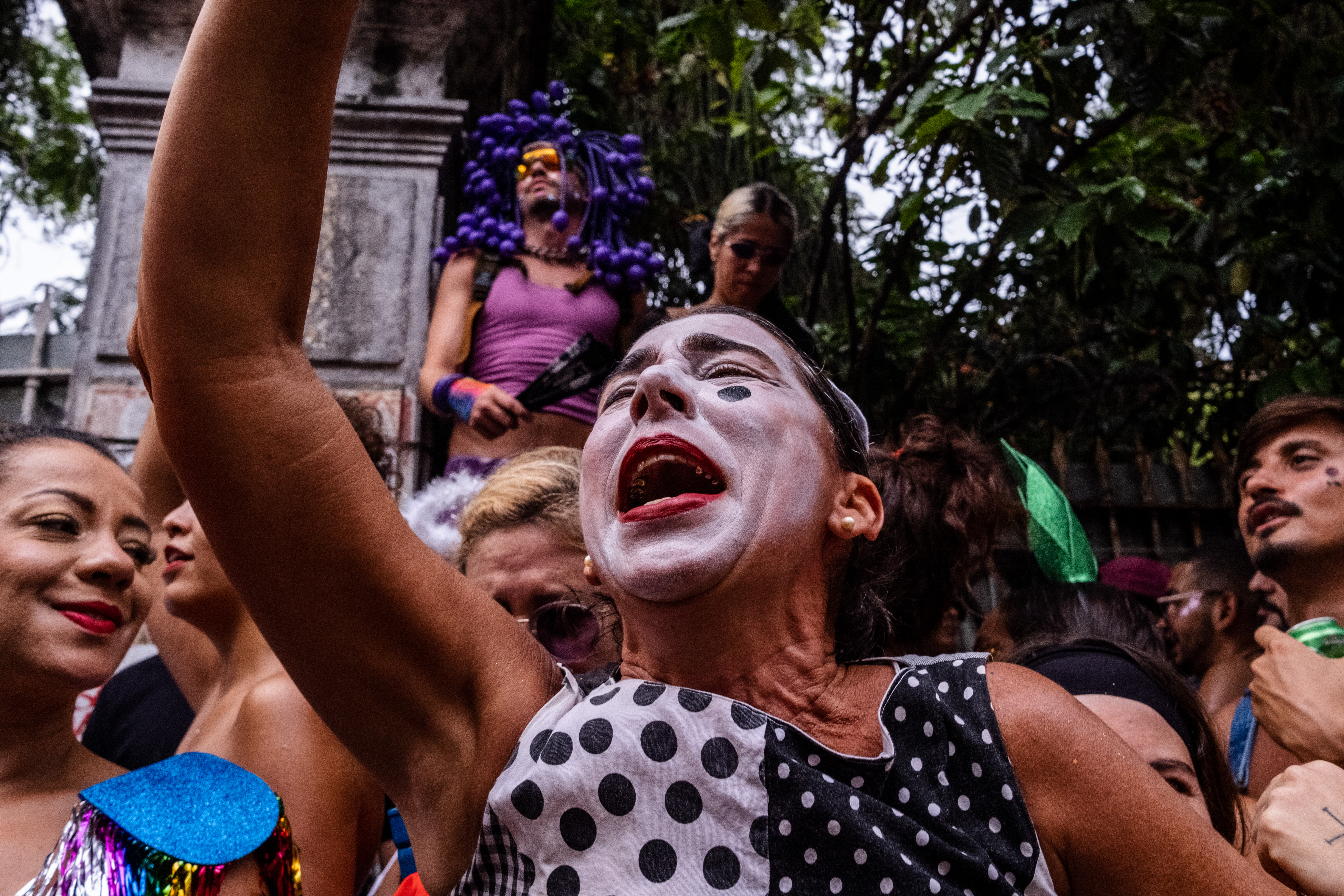 A woman in mime makeup joyfully screams on a crowded sidewalk.