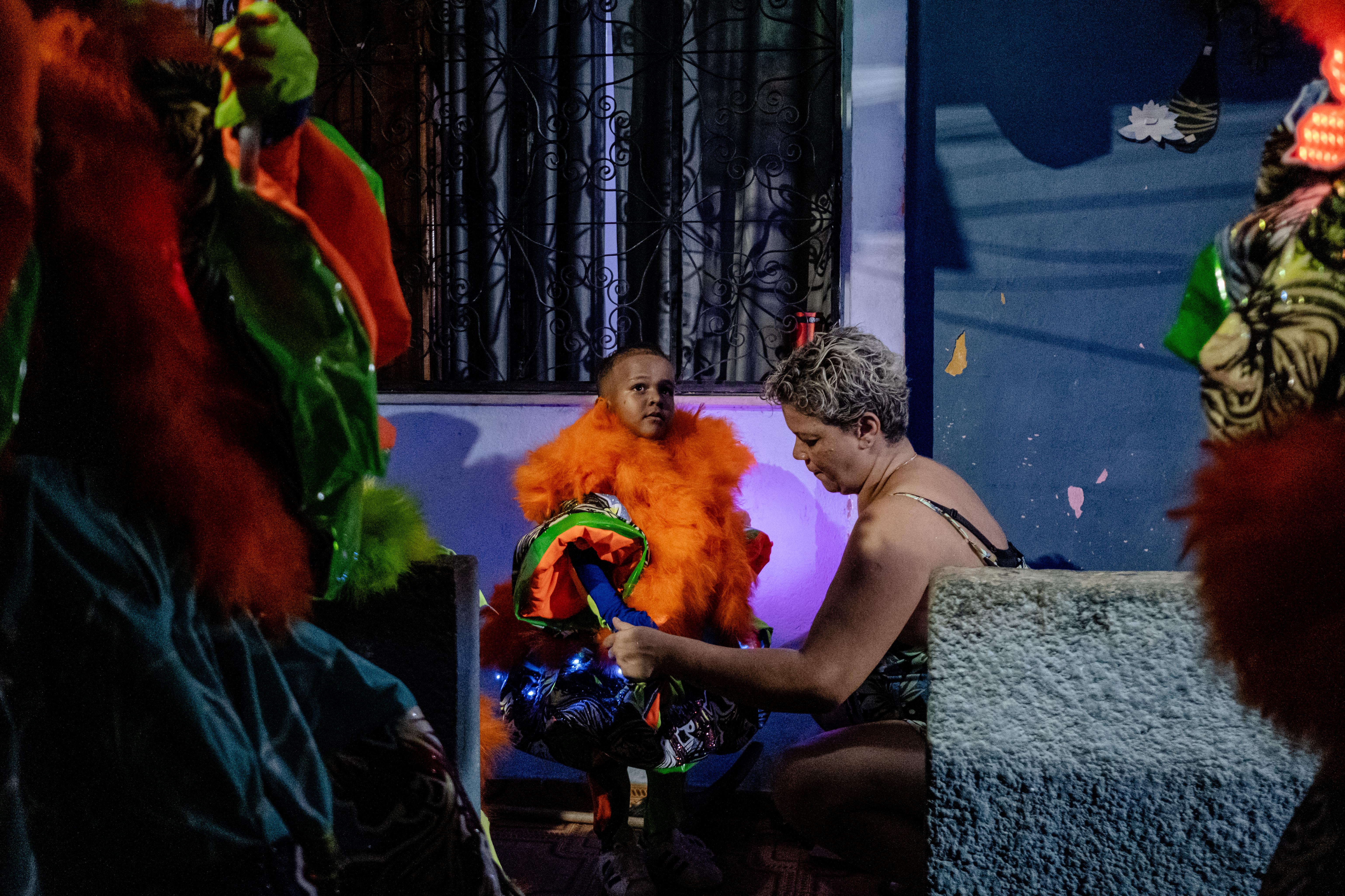 A young child is being fitted with a colorful traditional costume by a woman.