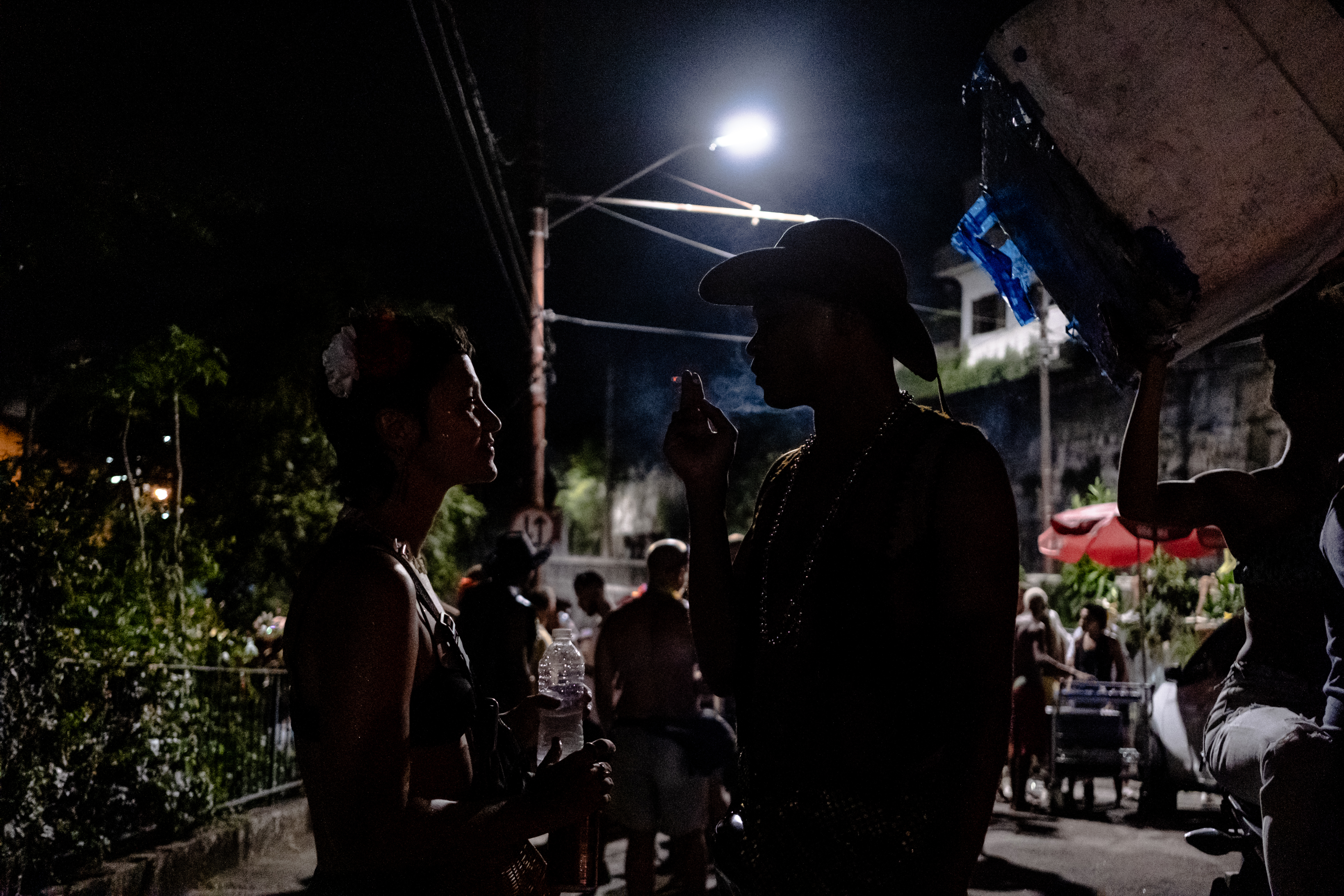 Two people chat under a streetlight at night, one of them is smoking and they're both silhouetted.