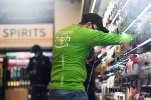 An Amazon Fresh employee wearing an Amazon shirt stocks shelves in a Just Walk Out store. Behind them is the liquor and alcohol section.