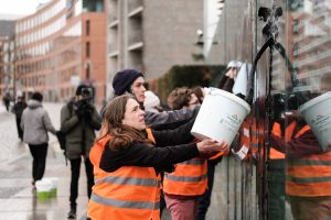 Menschen in Warnwesten kippen Eimer mit Öl auf Glastafeln, Aktivisten der Letzten Generation haben am Wochenende aus Protest das Kunstwerk "Grundgesetz 49" mit Öl beschmiert.