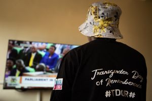 A Ugandan transgender woman who was recently attacked and currently being sheltered watches a TV screen showing the live broadcast of the session from the Parliament for the anti-gay bill​.