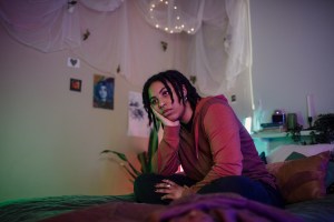 Thoughtful non-binary person looking away while sitting on bed at home - stock photo