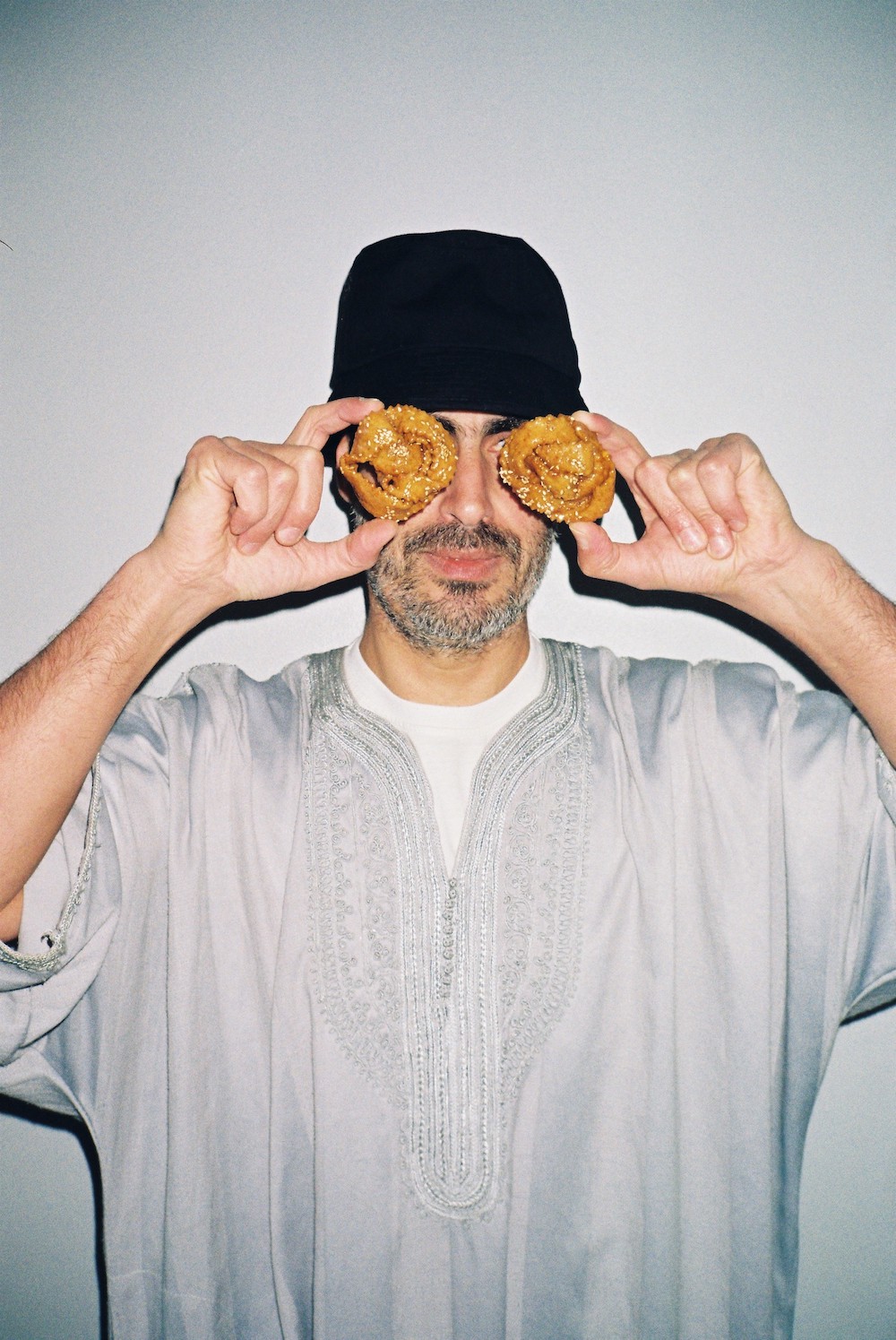 Ramadan photos. A man wearing a grey jellaba and a black hat holds two chebakias in front of his eyes