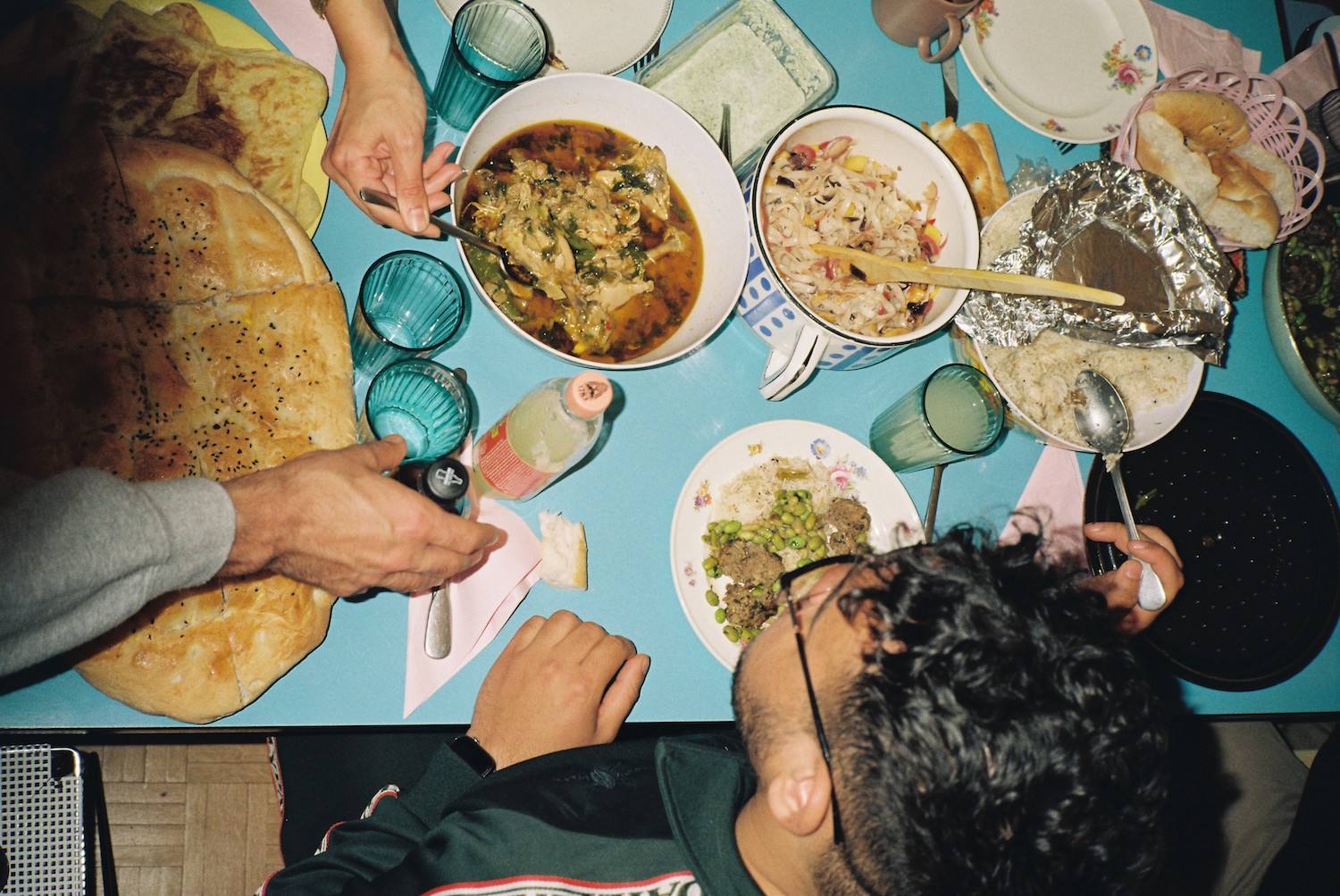 Ramadan photos. A blue table with loads of food on it including bread. Hands are serving food and we see the head of a young man.