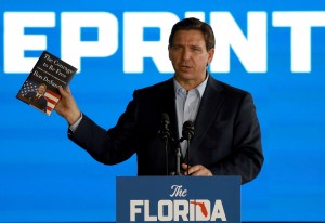 Ron DeSantis standing at a podium holding a ca book