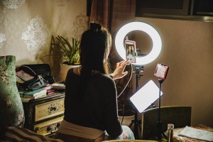 A woman sitting in front of two tripod-mounte smartphones op statieven en ring light