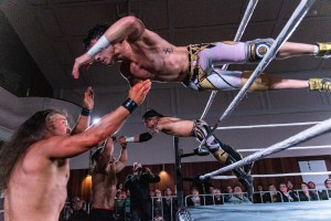 Two wrestlers dive out of the ring.