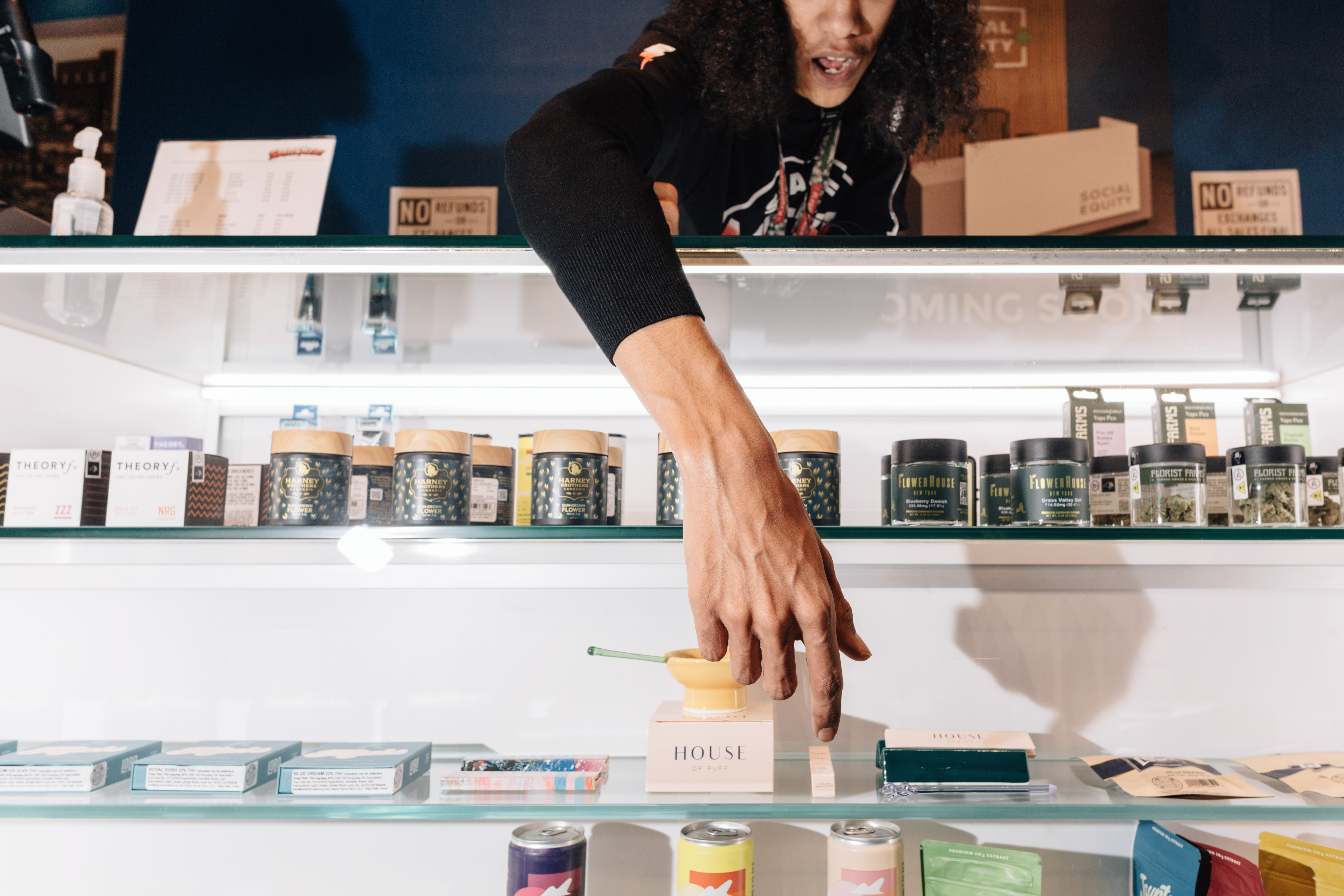 A budtender's hand is seen pointing to a display case filled with weed products.