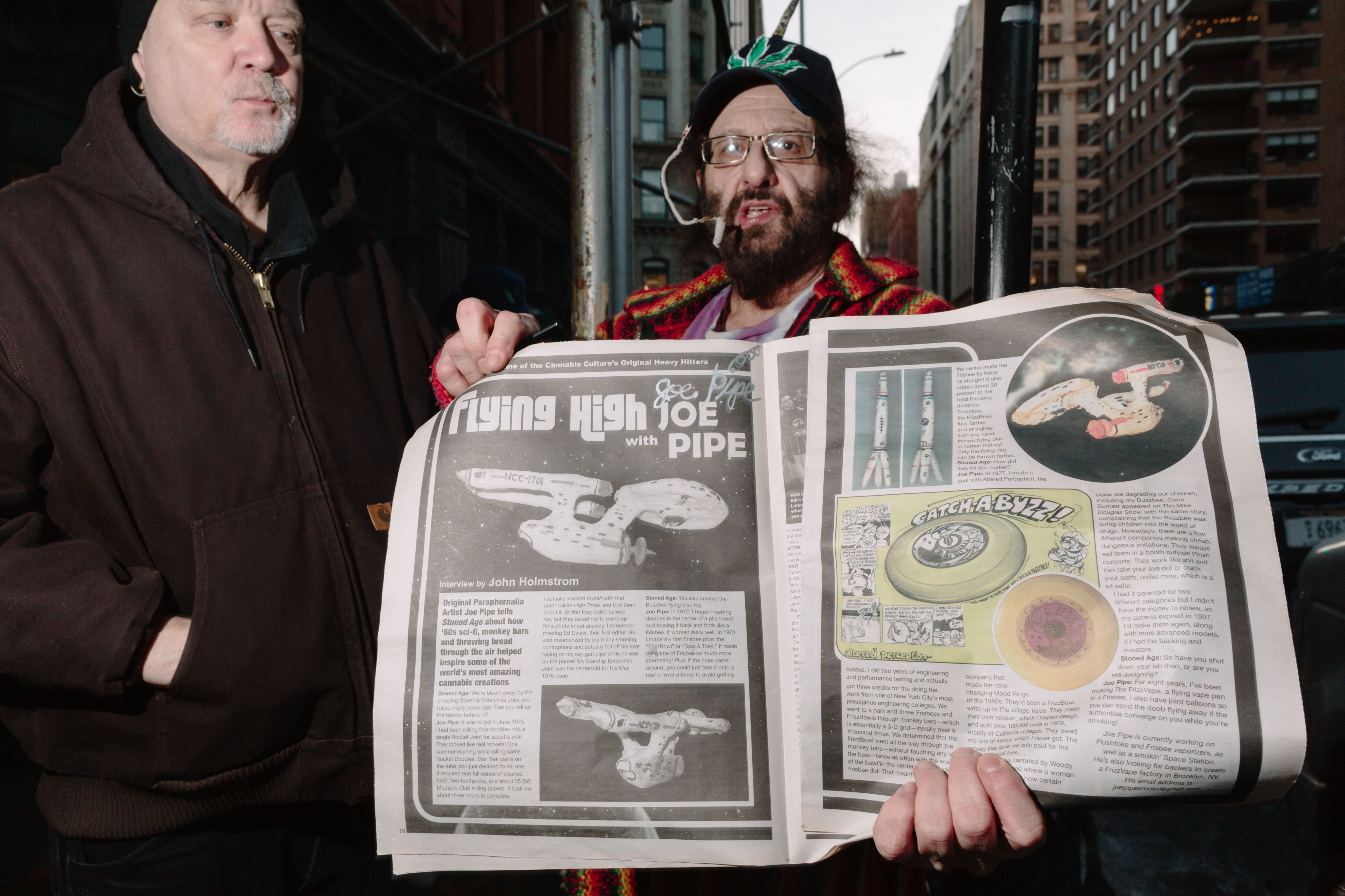 A man with a weed hat and a roach clip attached to it holds a spread out newspaper that reads Flying High with Joe Pipe. An image of the Star Trek Enterprise ship is printed .