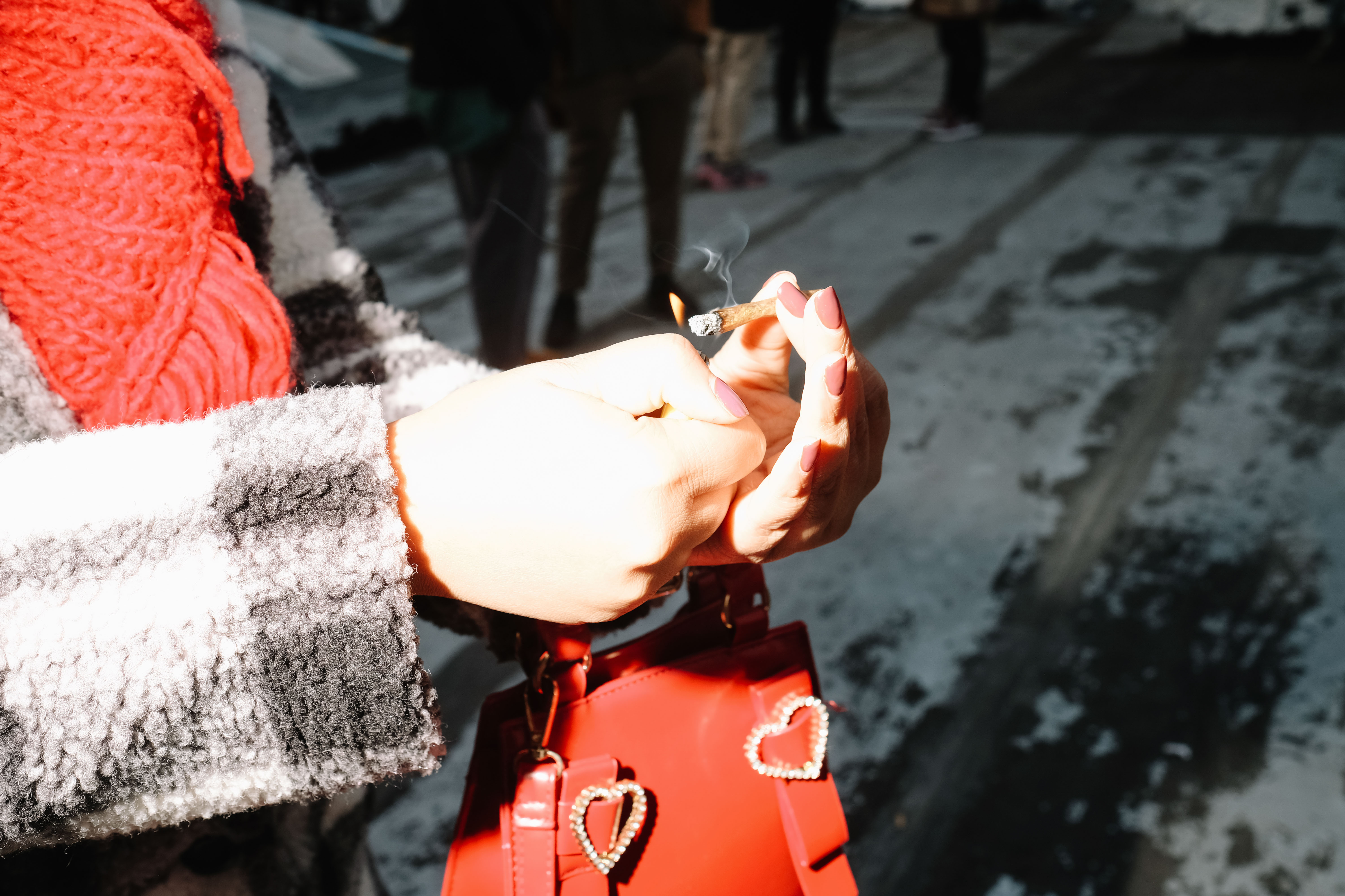 A woman with red nails, red scarf, and red purse lights a joint.