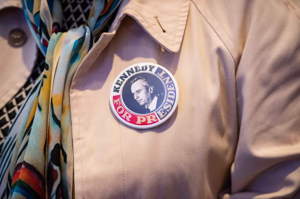 ​A support of Robert F. Kennedy Jr. wears a pin with his face on it at his presidential campaign announcement in Boston. Photo via Getty Images