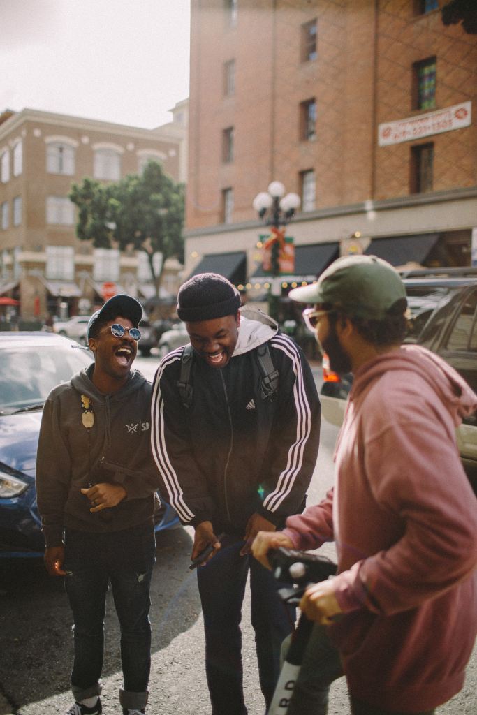 Friendship – three men standing near cars in a town centre and laughing.