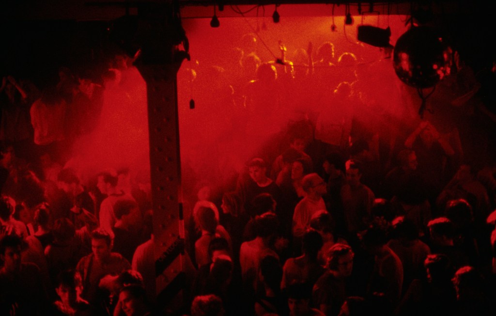 A crowded club lit only by deep red lights.