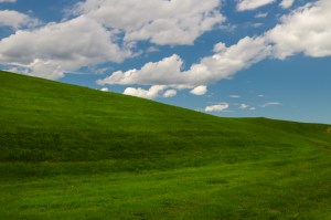 A blue sky with clouds with a green field below