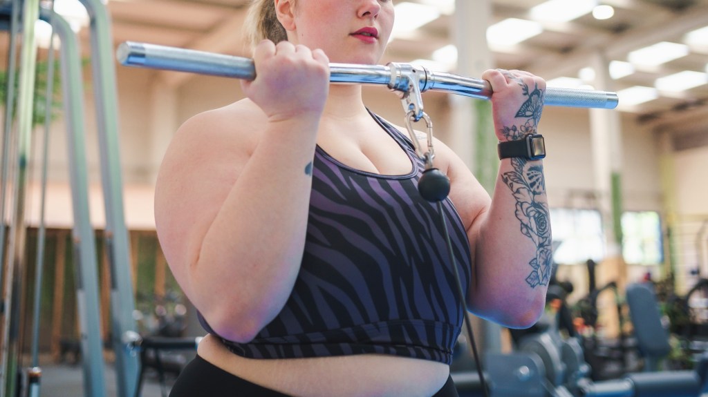 A photo of a large, curvy white woiman in the gym holdifor