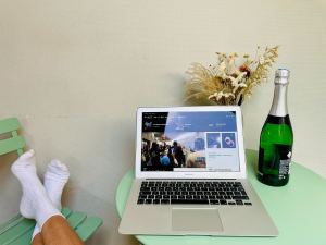 Photo of a small mint-green table and chair set with a Macbook and a champagne bottle on it. Someone is putting up their feet on the chair and leaning back off camera.