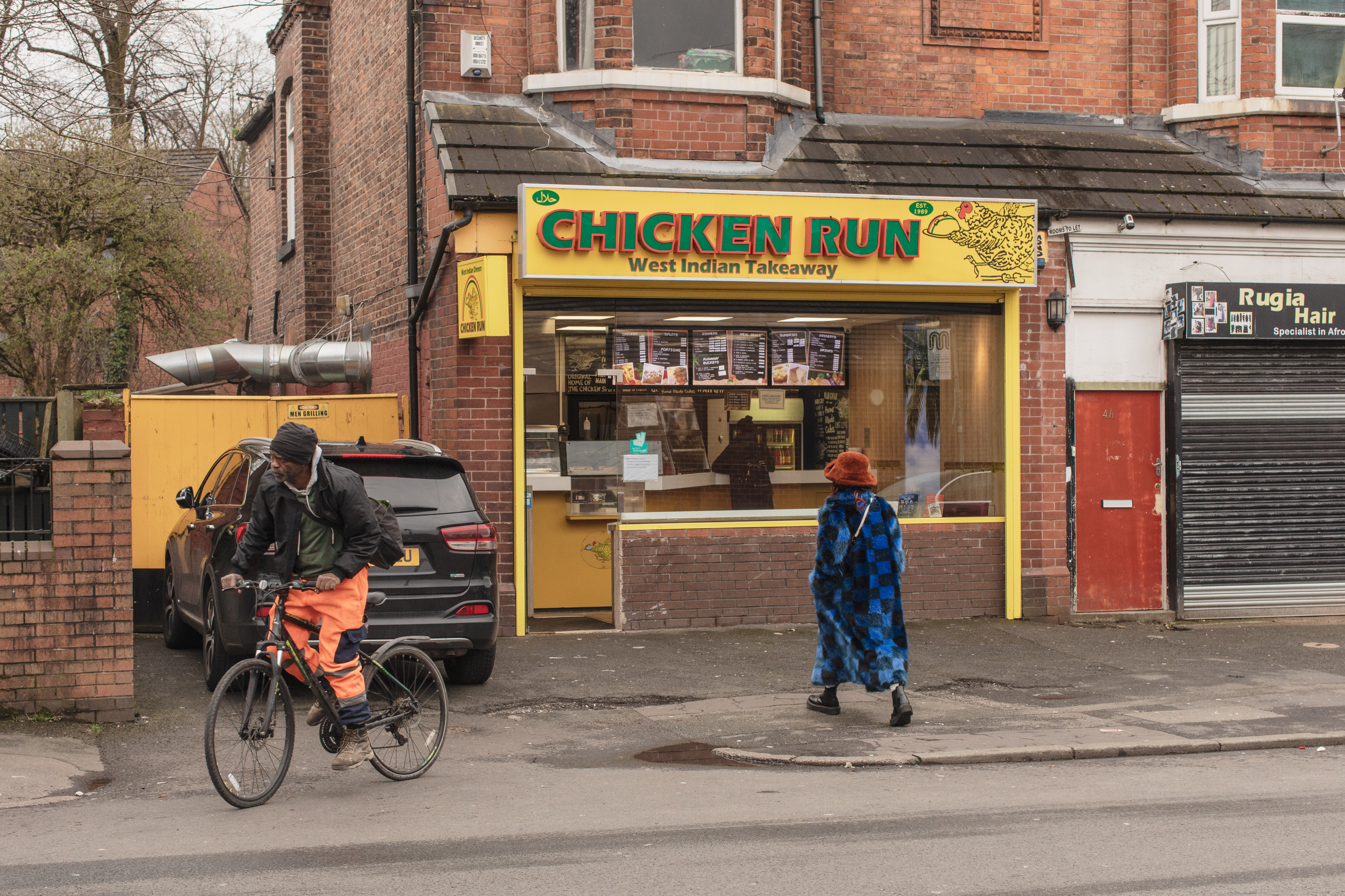 Manchester, UK: Woman in blue fur coat walks towards Chicken Run takeaway.