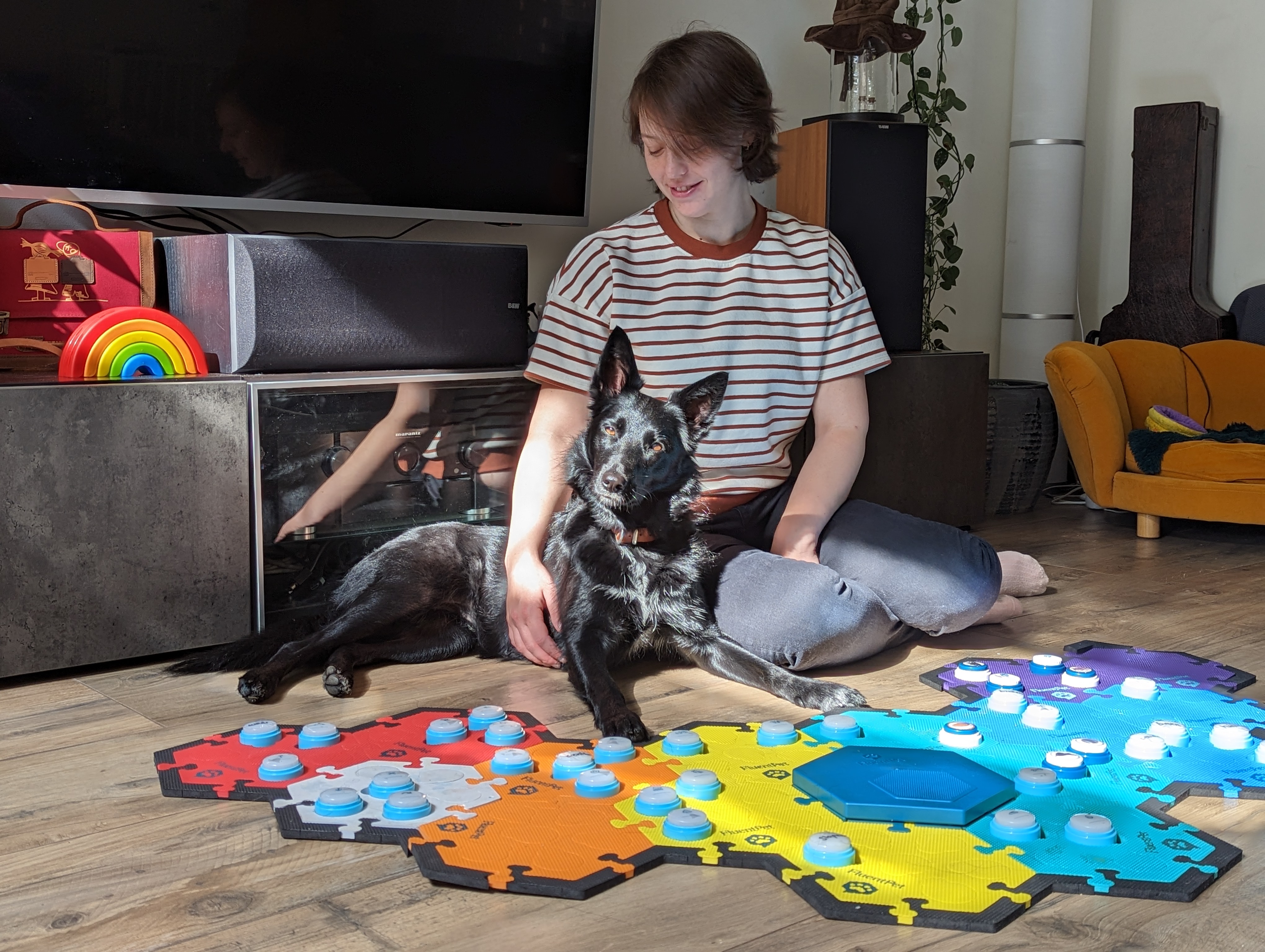 Silke and Karlijn Koning, talking dog – black dog lying on the ground next to her owner in front of a colourful mat with different sound buttons