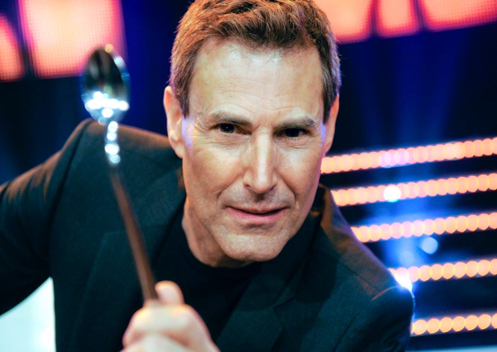 Uri Geller guckt skeptisch und hält einen Löffel ins Bild. In dem Artikel geht es um Uri Geller und Aliens.