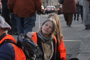 Caroline Schmidt von der Letzten Generation klebt auf der Straße. Sie trägt eine orange Warnweste.