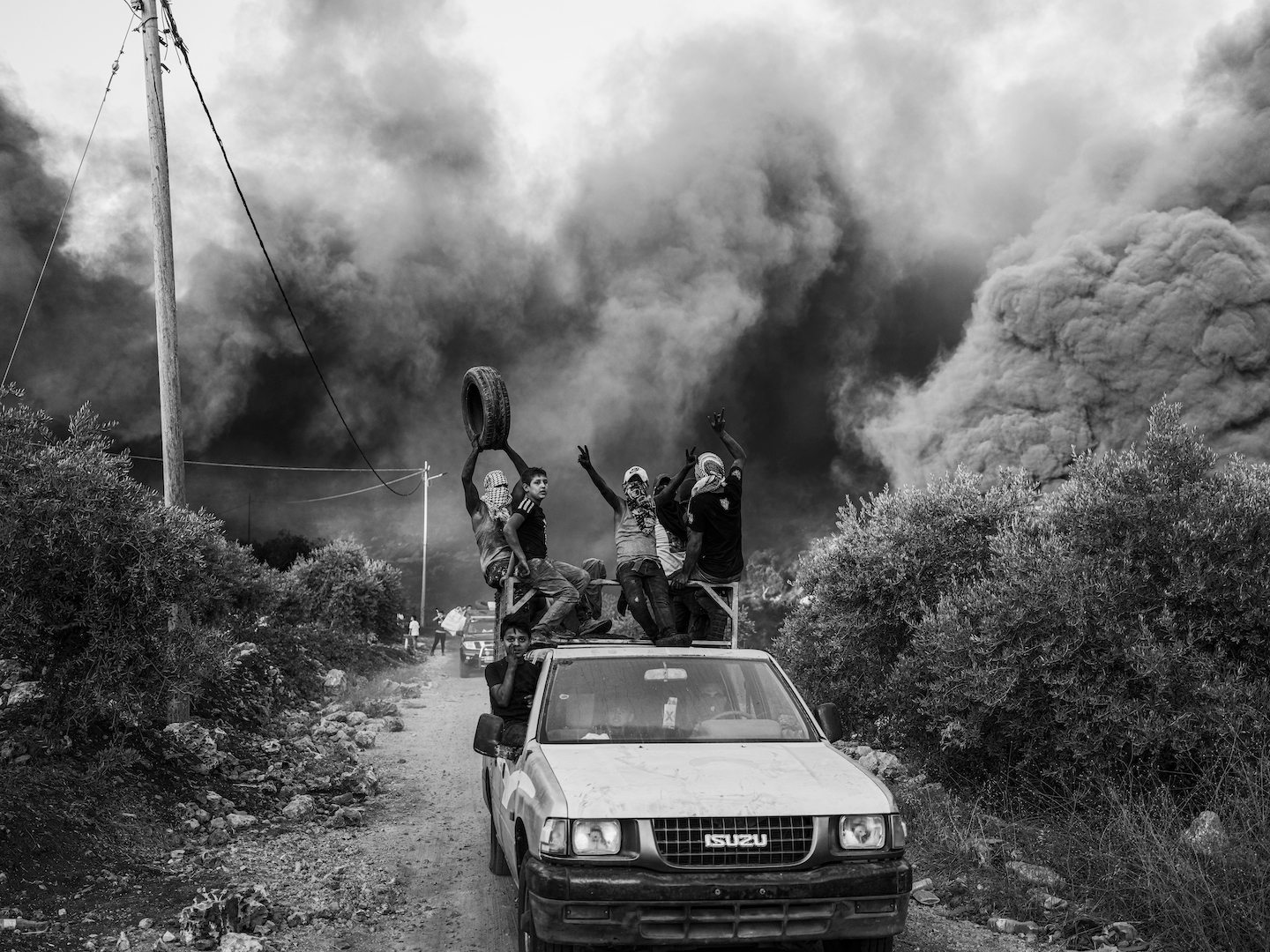 A group of people are crowded into a car and also ride on its roof, with their hands raised in the air.