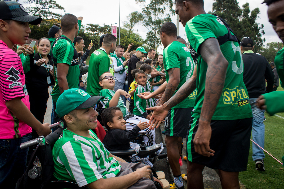 Football players in green shake hands with supporters with disabilities.