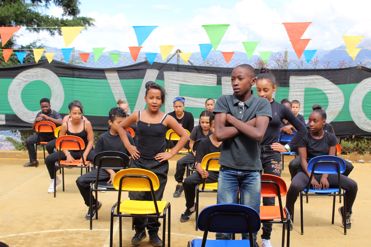 Group of kids sitting on chairs in front of a large Pueblo Verdolaga banner.