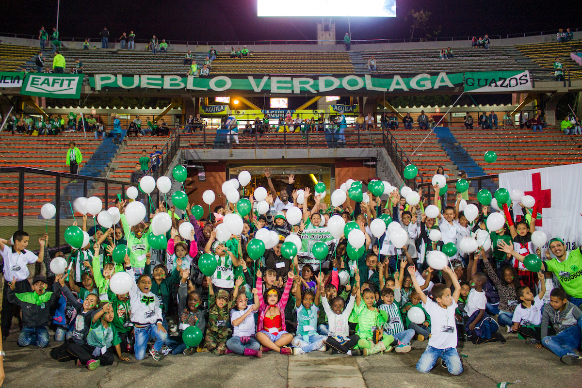 Kids holding green and white balloons in a football stadium.