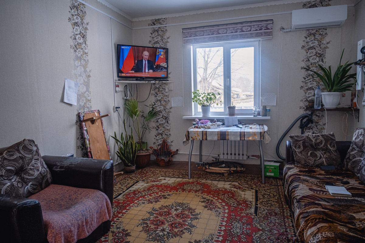 François Artusse, Udege people Russia – living room with highly decorative carpets, wallpaper and sofa covers. In a corner, a small TV is playing footage of Putin