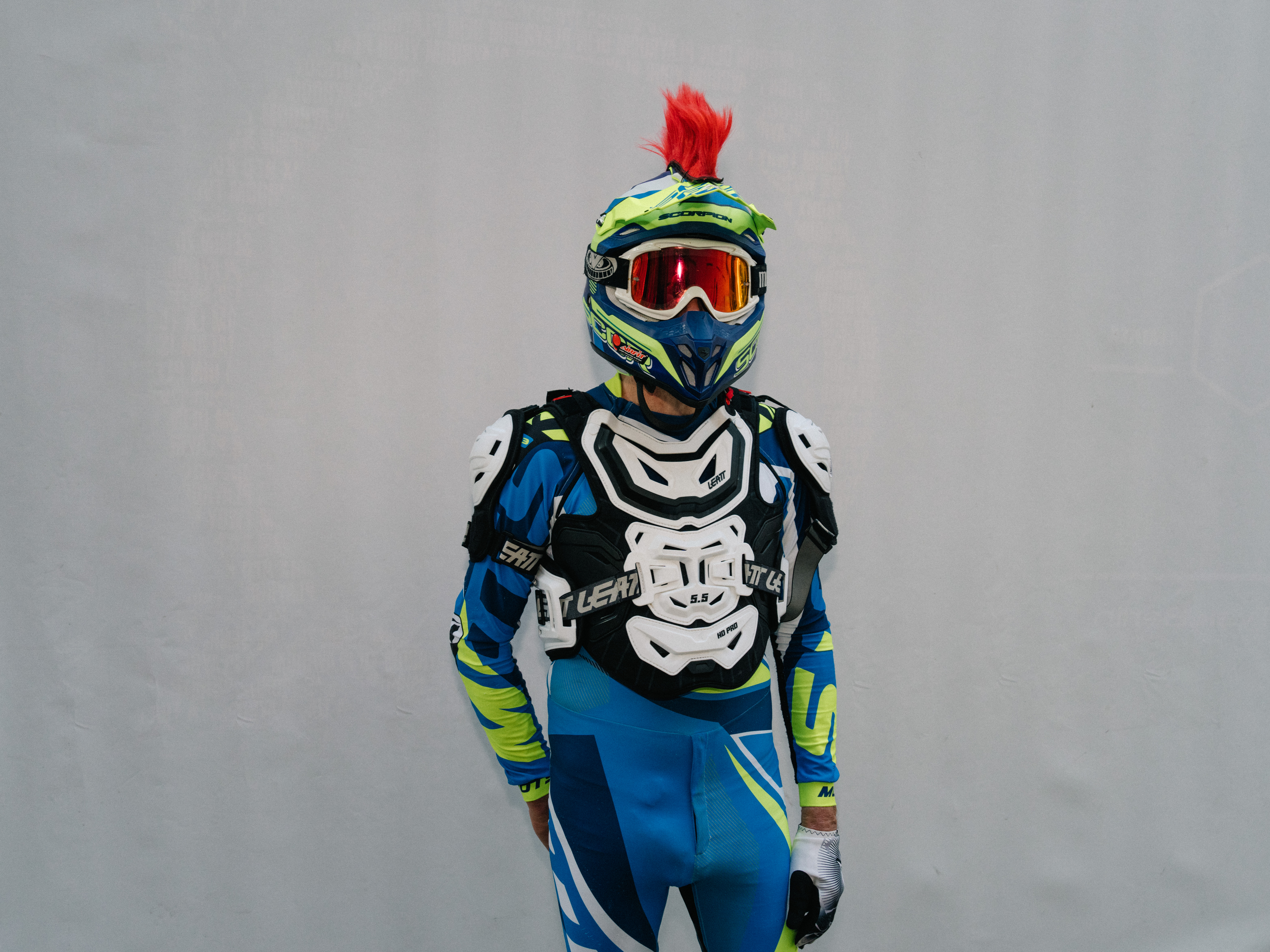 A man wearing a blue, white and green motocross outfit with helmet and an orange ski mask.