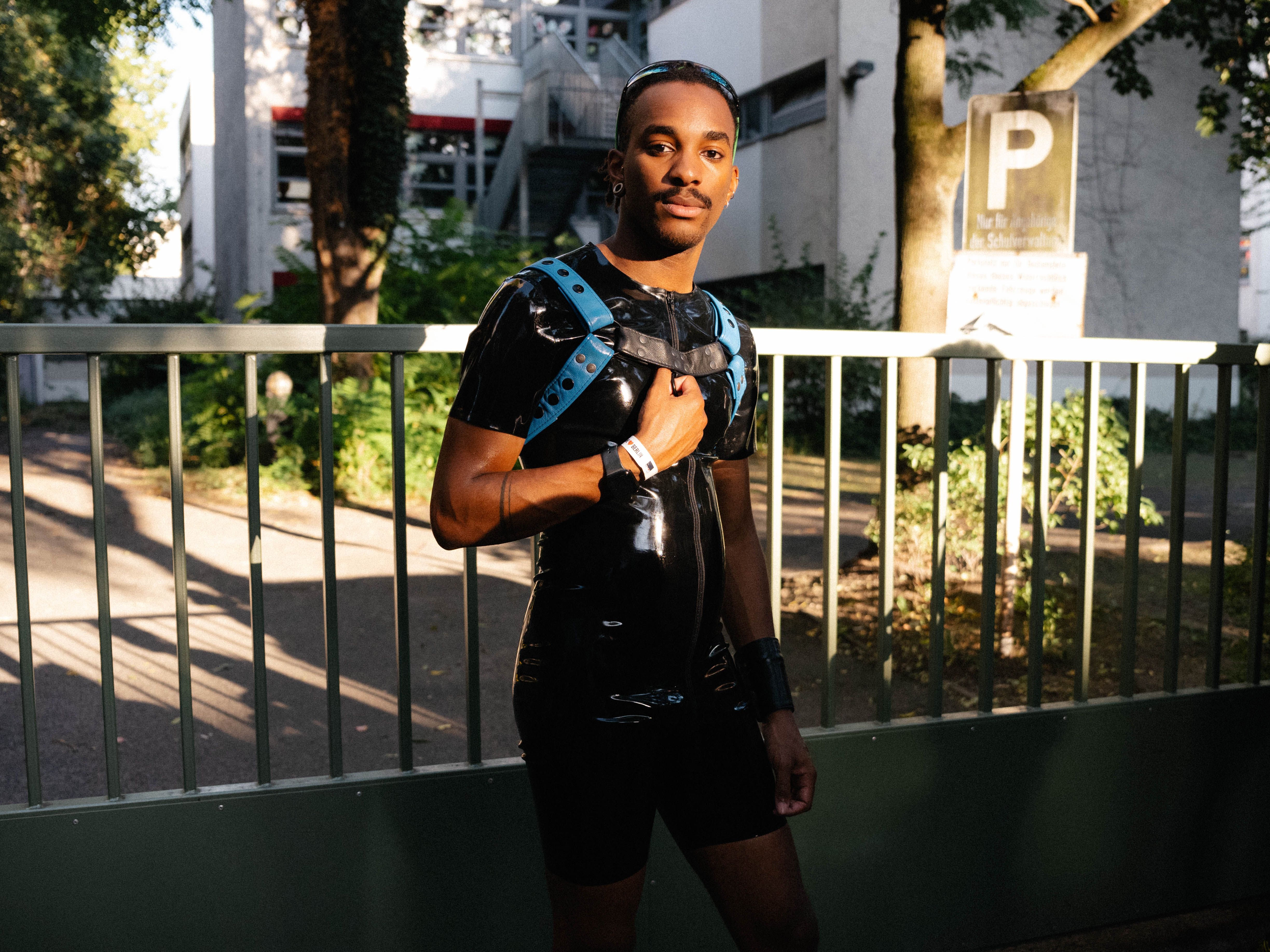 A person in a short-sleeved, black latex jumpsuit with shorts and a black and blue harness.