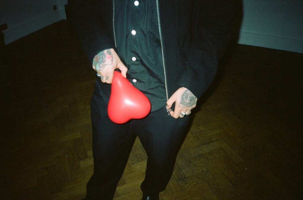 Man with tattoos holding heart-shaped balloon filled with laughing as