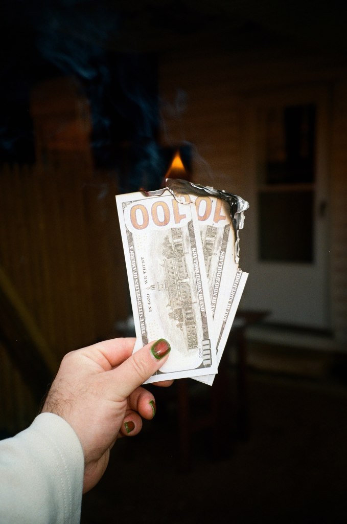 Person with painted nails holding burning cash