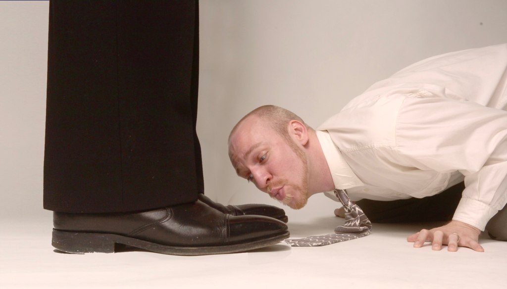 Man in office attire kissing someone else's shoes