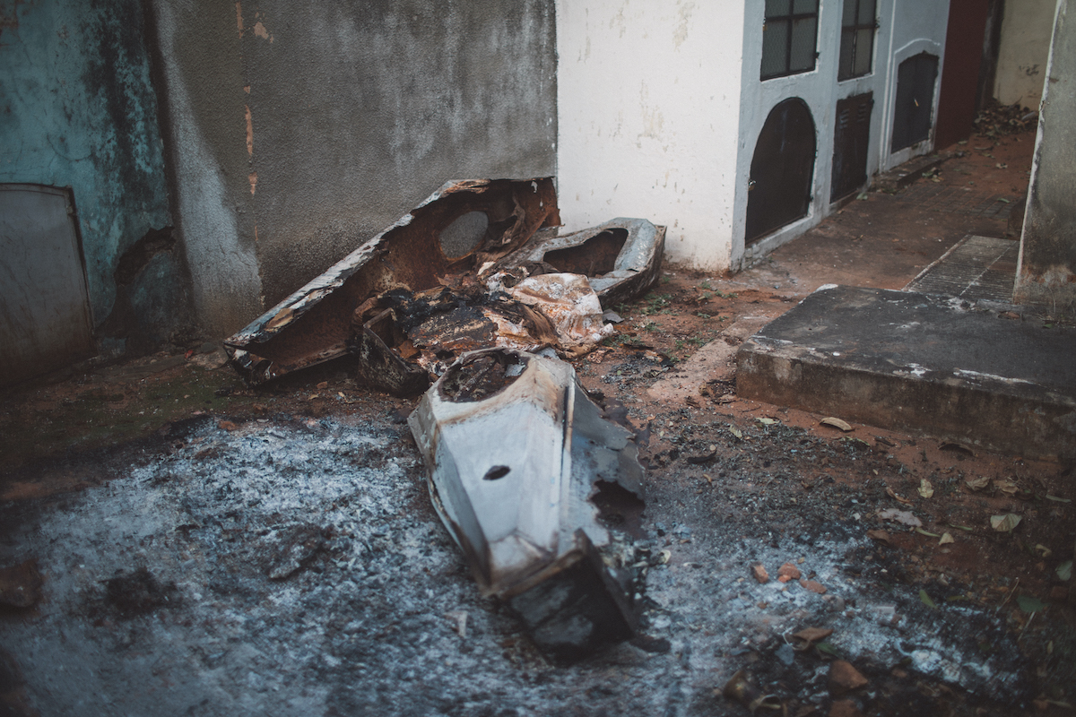 A photo of two burnt up caskets abandoned in an alleyway and surrounded by ashes.